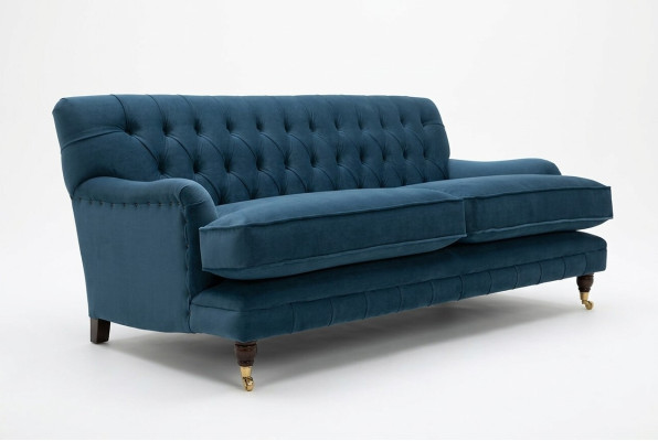 Zils mūsdienīgs Chesterfield trijosvietu luksusa dīvāns dzīvojamās istabas gultā.